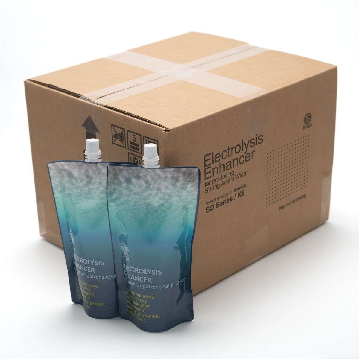 Two flexible pouches labeled Electrolysis Enhancer are standing in front of a large cardboard shipping box with printed details and handling symbols.